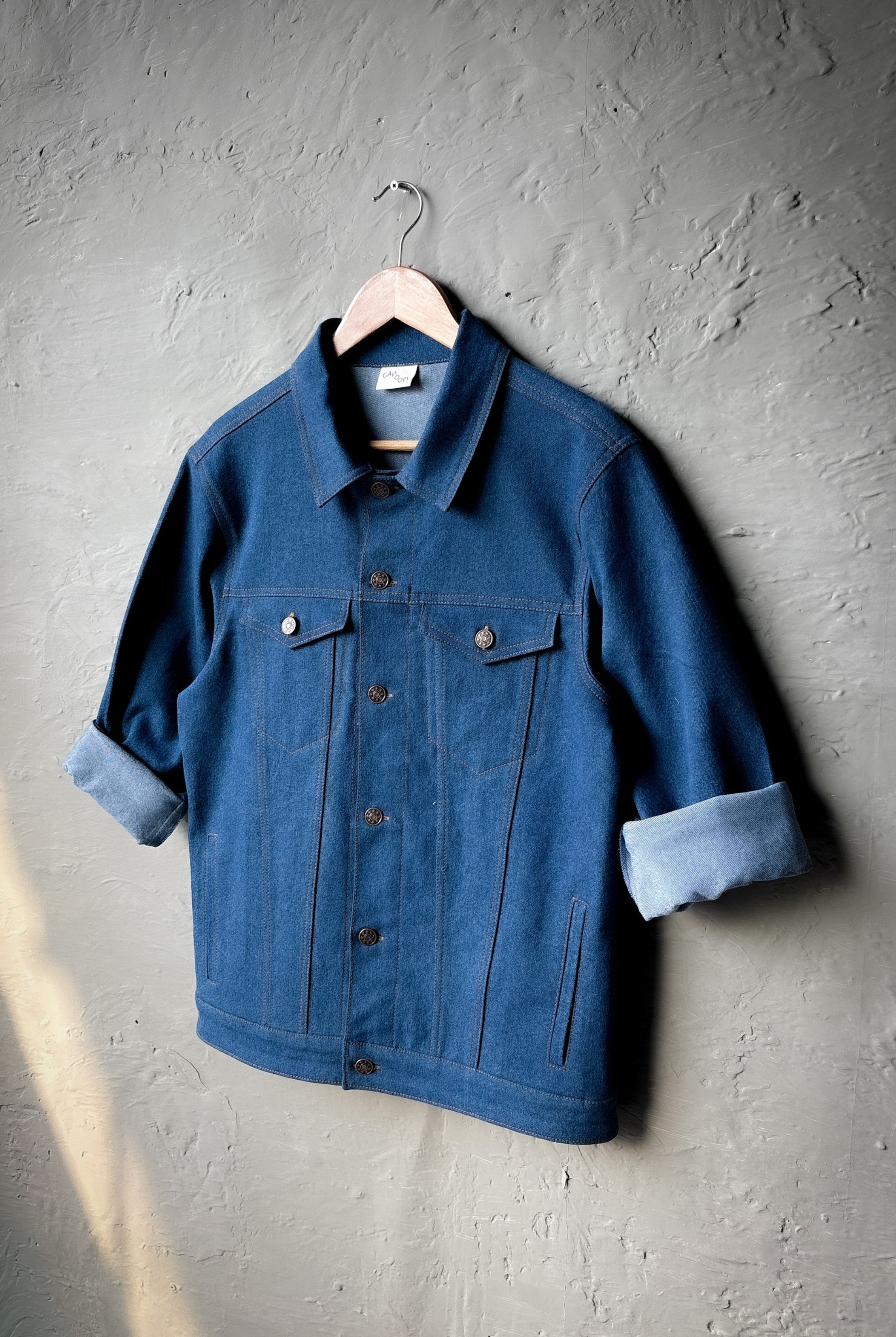 Blue denim jacket on a hanger against a gray textured wall